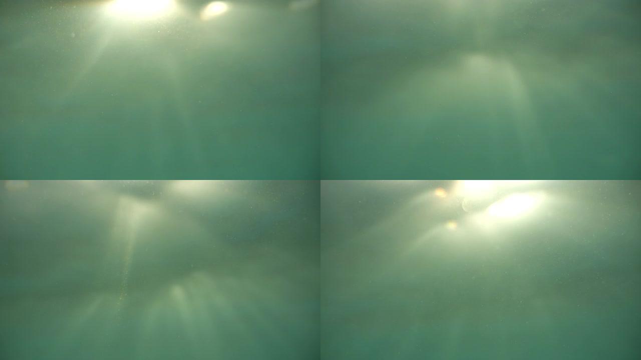 从下面看水面。重点关注水中漂浮的沙粒、磷虾和气泡，这些沙粒被太阳光线背光照射。靠近水面和水深的气泡。