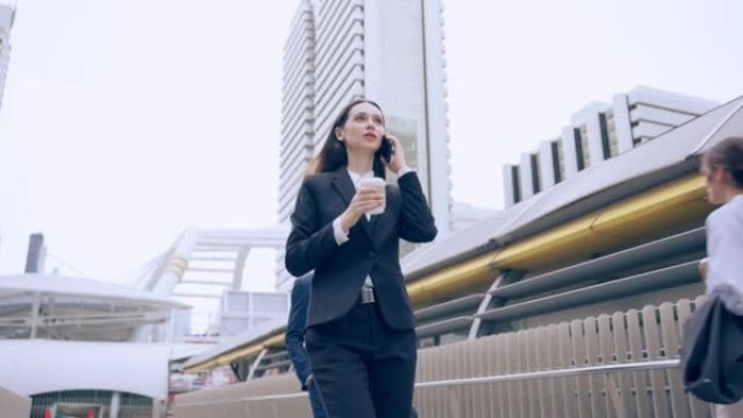 白人年轻女商人在城市散步时用智能手机聊天。迷人美丽的女员工拿着咖啡，自信地在户外与同事进行手机交流。