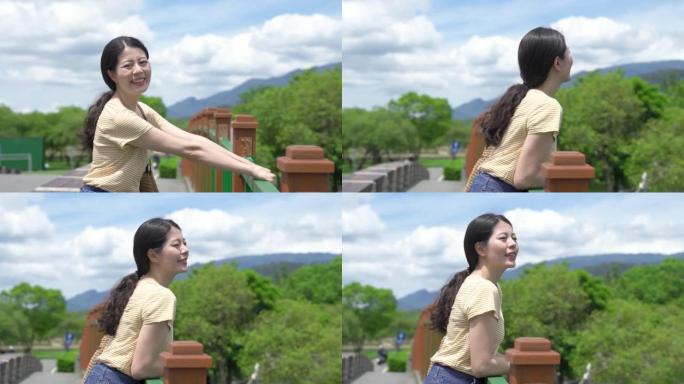 可爱的台湾女士挂在扶手上，对着镜头微笑，一边欣赏大坡湖阳光下桥上的美景。