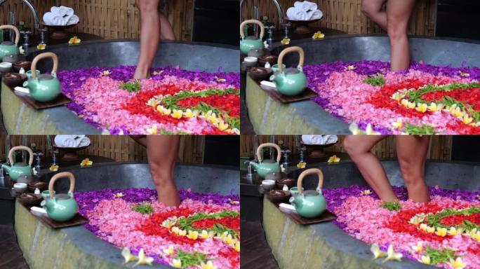 一位女士轻轻地将双腿伸入充满各种花朵的浴缸中。在水疗酒店的香薰假期将迅速预见您与您的身体和精神和谐相