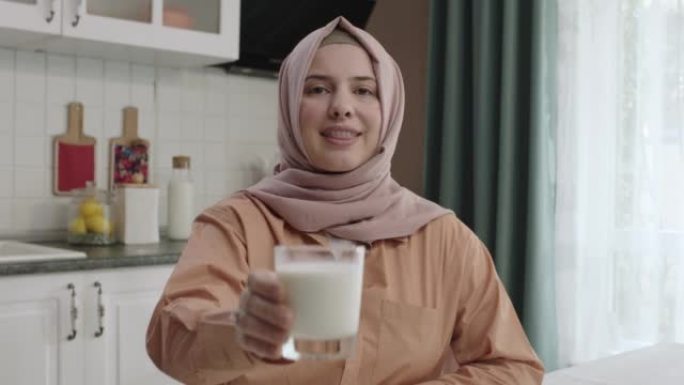 戴头巾的女人给相机一杯牛奶。