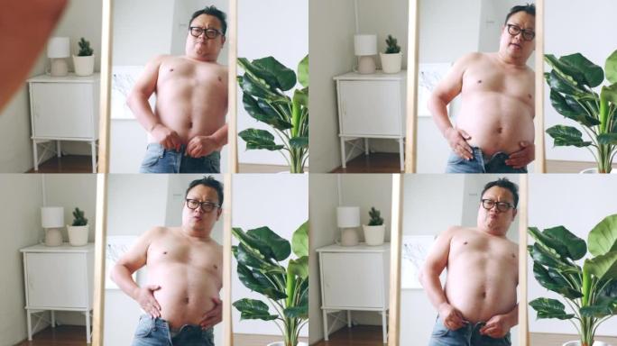 大肚子的亚洲胖子看着镜子里的身体反射，担心肥胖的身体