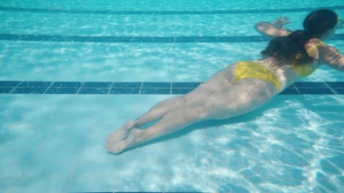 一个穿着黄色泳衣和面具的女孩在游泳池里，在水下游泳。慢动作。游泳池和水下相机。