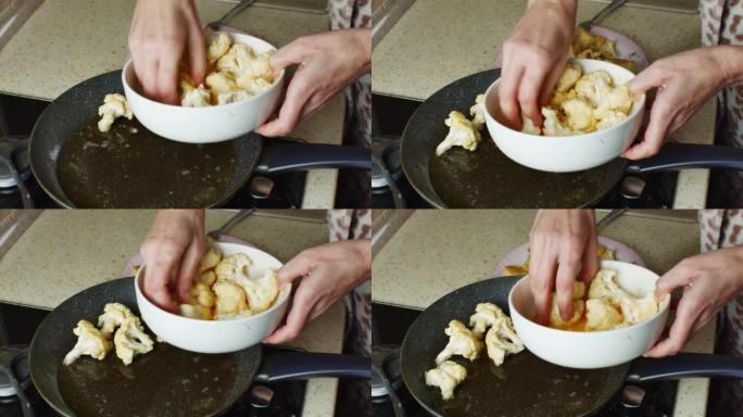 一个女人的手的特写镜头将花椰菜块放在碗里的打好的鸡蛋面糊中，放入装有葵花籽油的热锅中。一位家庭主妇在