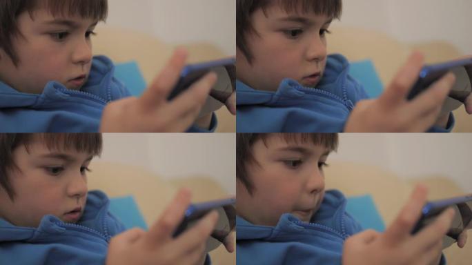特写镜头孩子在家沙发上玩手机游戏。男孩在手机上玩电子游戏。学龄前儿童在沙发上玩电子游戏智能手机。儿童