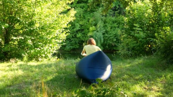 女人在野外露营的充气沙发上放松。大自然中的空气沙发或Lamzac。绿色森林和河流。