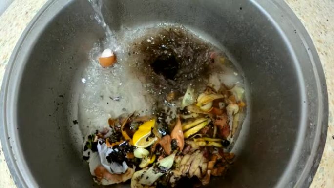 厨房水槽里的食物垃圾。剩下的食物是可回收的废物。厨房技术-食物垃圾粉碎机。水流慢动作。食物垃圾被压入
