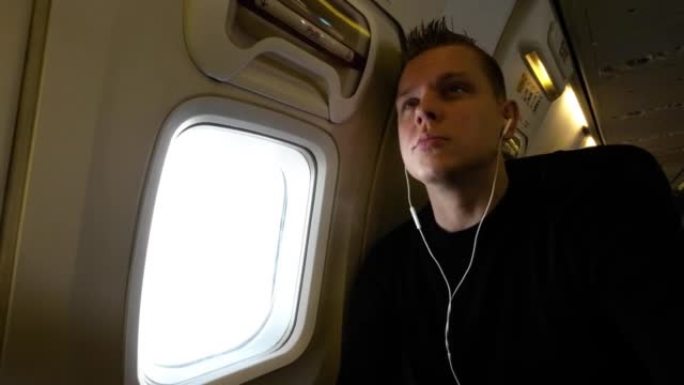 年轻的白人男性，带着耳塞看着相机，看着飞机上的窗外