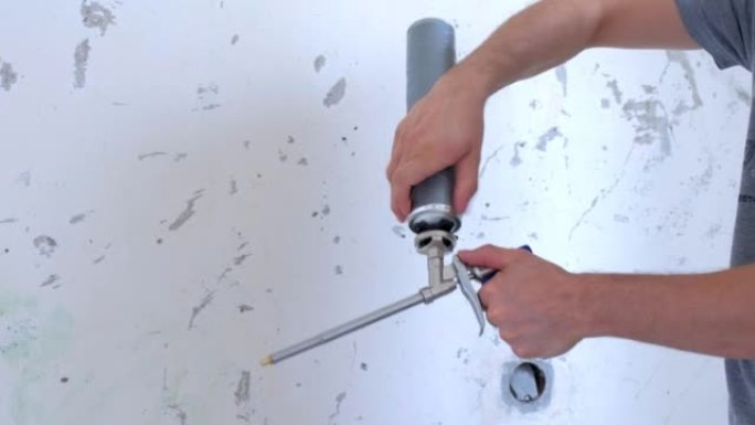 男子建筑工人将一瓶安装泡沫拧到工具上，双手特写。