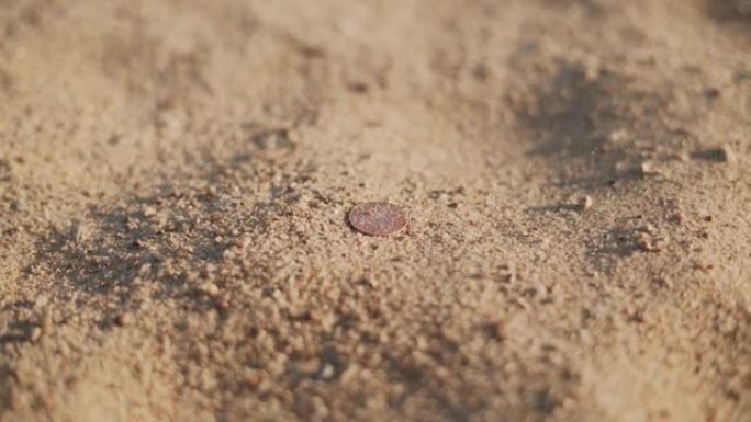 圆形硬币躺在沙子上。支付手段覆盖着沙子。