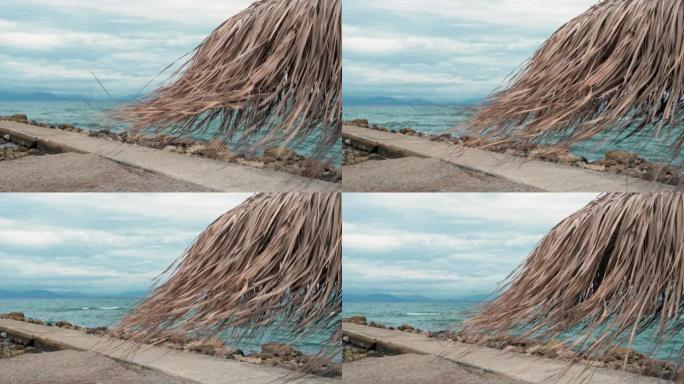 棕榈叶制成的沙滩伞在码头，爱奥尼亚海，Moraitika，科孚岛，希腊的背景下随风摇摆。度假村恶劣天