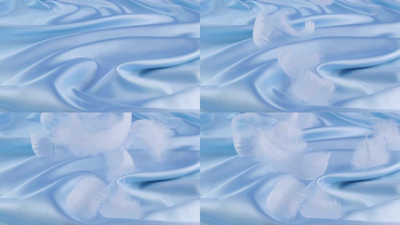 白色的天鹅羽毛落在蓝色的丝绸上。慢动作。