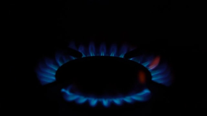 厨房炉子上的煤气灶亮了起来。黑色背景上燃烧着蓝色火焰。天然气发炎。天然能源载体，化石燃料