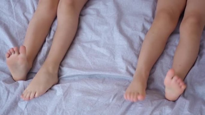 儿童脚的特写。两个小孩躺在床上把腿晃来晃去。