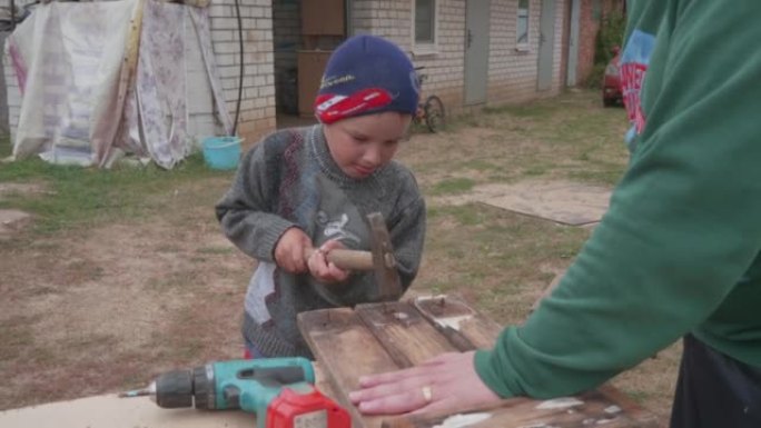一个孩子用锤子从木板上敲出旧钉子。一个小男孩帮他爸爸打掉生锈的指甲。父子之间的信任、爱和亲密。