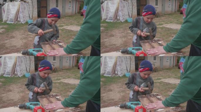 一个孩子用锤子从木板上敲出旧钉子。一个小男孩帮他爸爸打掉生锈的指甲。父子之间的信任、爱和亲密。