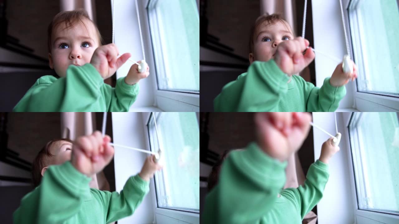 好奇的活跃的高加索孩子从jalousie窗帘上拉着绳子。男婴站在窗前玩耍，兴致地抬头。特写。