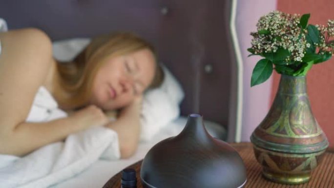 一位年轻女子睡在床上，享受着香气扩散器营造的氛围。灯在前景。芳香疗法概念。电动超声波精油芳香扩散器和
