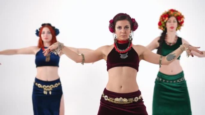三个苗条的女人在慢动作中跳舞弯曲身体，表演肚皮舞。白人灵活自信的舞者在白色背景下表演中东舞蹈。