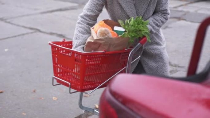 一个女人把杂货放在车里。超市里有杂货的手推车。