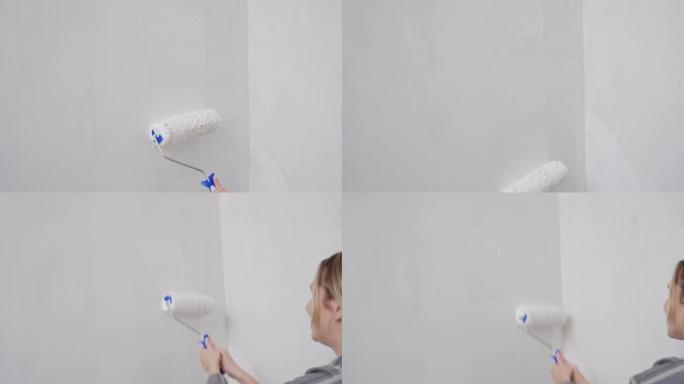 女性手的特写镜头驱动墙壁上带有白色油漆的油漆滚筒。修理，墙面粉刷