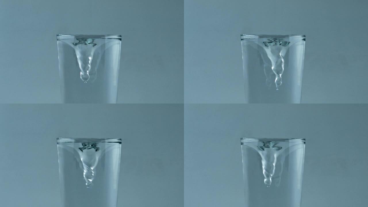 玻璃容器内透明冷水涡流特写。冰鸡尾酒纺纱
