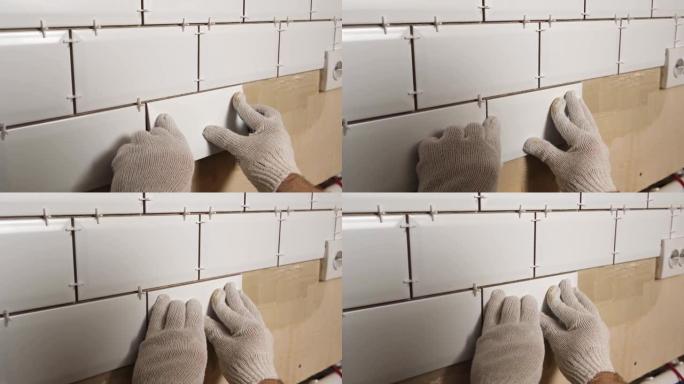 男工师傅在厨房墙壁上铺设瓷砖。修理工放置白色现代瓷砖，铺展粘合剂。建筑商在维修翻新工作中安装瓷砖。专