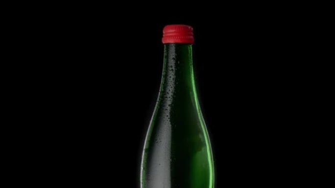 绿色一瓶红色瓶盖的矿泉水。水滴中的玻璃瓶在黑色背景上旋转