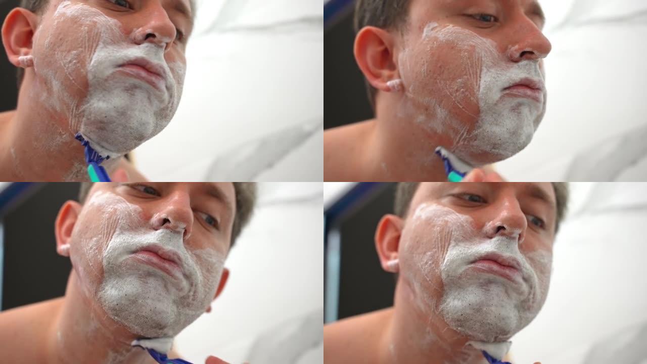 英俊的男人在浴室使用一次性剃刀刮胡须和胡须，男人在剃须前在面部皮肤上涂抹保湿泡沫。日常美容护理，男士