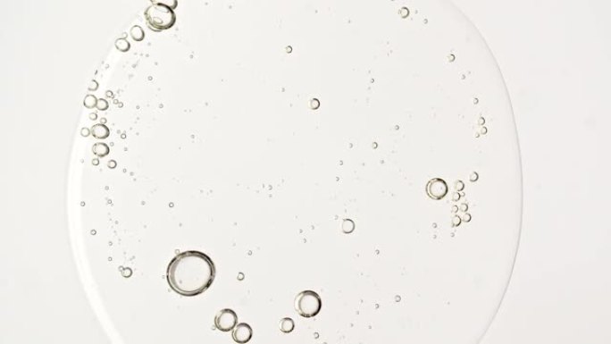 透明化妆品凝胶液，带有分子气泡的血清油在移液器中滴落在白色背景上。天然有机化妆品、药物的宏观拍摄。生