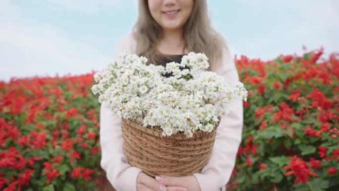 女人的笑脸走路，拿着白色雏菊的篮子。背景是一片红花