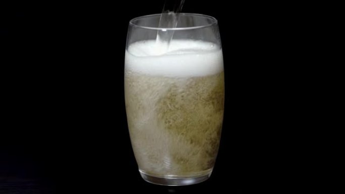 慢动作的碳酸汽水饮料倒入黑色背景的玻璃杯中