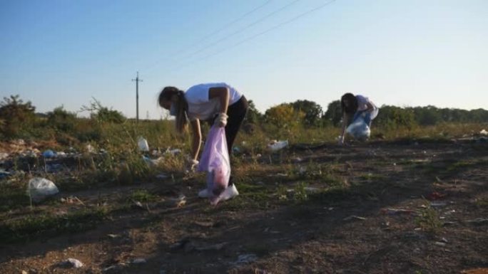 年轻的母亲和小女儿在农村清理塑料和纸张垃圾的草地。戴着口罩的生态志愿者家庭在路边附近的草坪上收集袋子