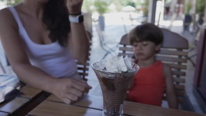 午餐后，母亲和孩子在餐厅用餐时分享冰淇淋甜点。甜甜点，上面放着鲜奶油