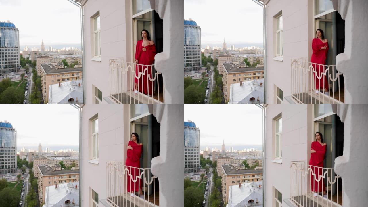 穿着红色丝绸长袍的女人在莫斯科高楼的阳台上出门。