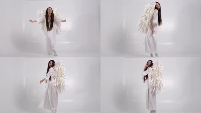 美丽的黑发女人，白色背景上有白色的翅膀。穿着天使服装的女孩。