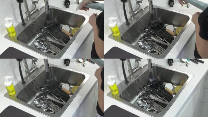 女人用海绵叉子洗勺子在厨房水槽里水流下，女人用手洗餐具特写。