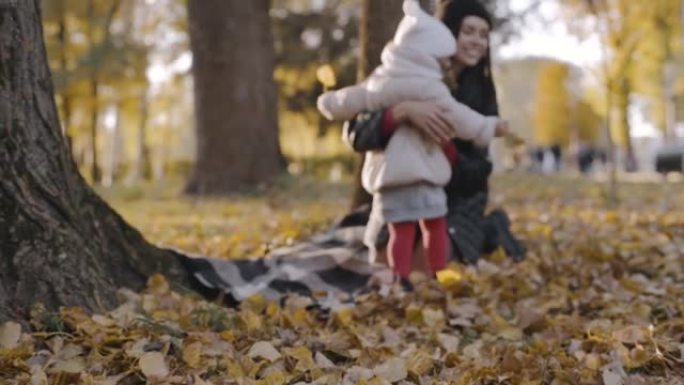 秋天公园里的小孩跑向妈妈，和妈妈一起生活，妈妈拥抱她的女儿。慢动作