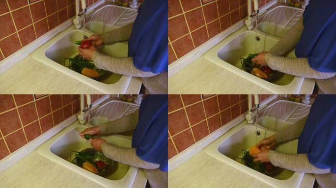 戴着头巾的穆斯林妇女的手特写，在厨房的自来水下洗水槽里新鲜的有机蔬菜