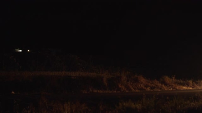 漆黑一片，一辆大灯点亮的汽车在乡村道路上经过