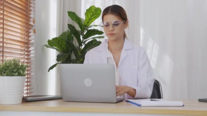 年轻的女医生一边在剪贴板上看文件，一边在诊所使用笔记本电脑，女性在医院使用笔记本电脑，一个人，医疗概