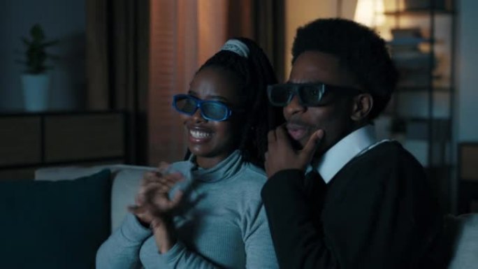 两个非洲外表的学生坐在沙发上看电影。他们戴上3D眼镜。这部电影的情节既有趣又出乎意料。年轻人情感讨论