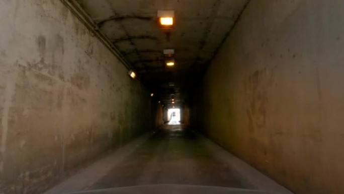 汽车通过旧混凝土隧道内的入口沿着道路和下坡行驶的前视图。