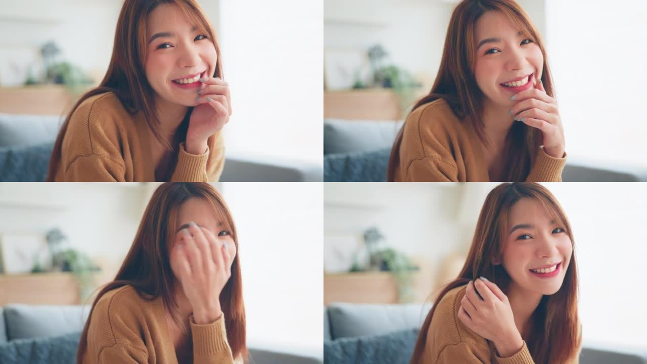 自信微笑的年轻亚洲女性坐在家里看着相机，快乐美丽的女士漂亮的脸牙齿微笑独自在室内摆姿势。