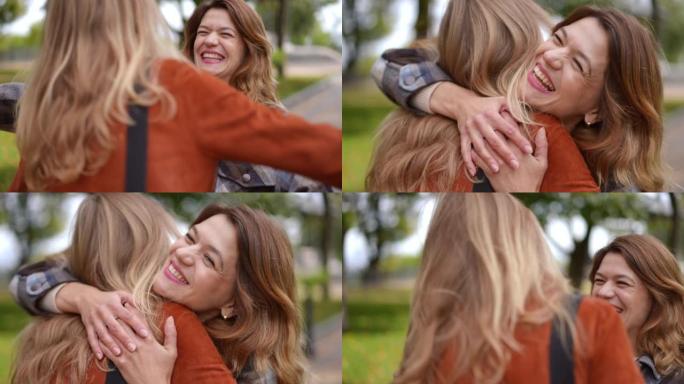 快乐的女人在秋季公园迎接朋友，拥抱在慢动作微笑。欢快美丽的高加索女士在户外欢欣鼓舞的肖像。友谊概念。