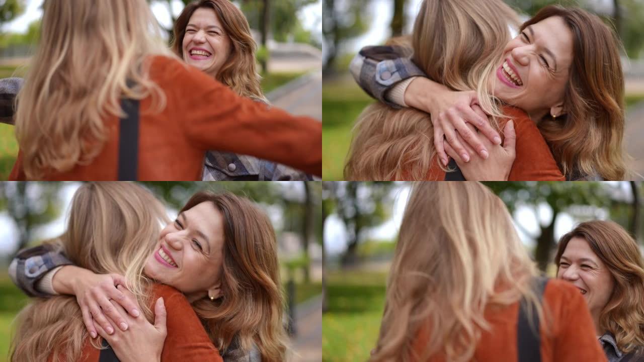 快乐的女人在秋季公园迎接朋友，拥抱在慢动作微笑。欢快美丽的高加索女士在户外欢欣鼓舞的肖像。友谊概念。