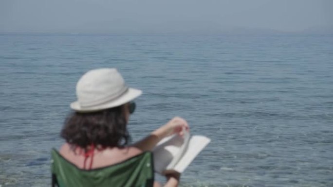 今年夏天会带来什么故事？美丽的女人在海滩上看书。模糊效应
