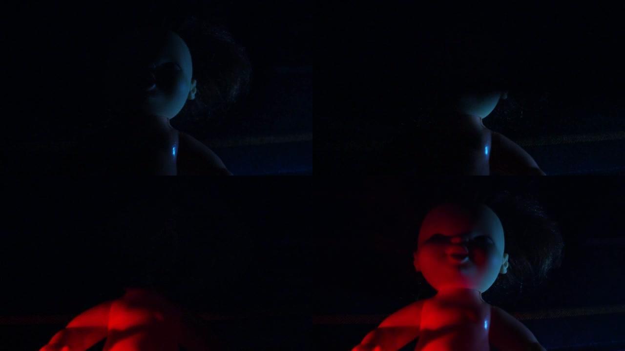 黑暗中有红色和蓝色灯光的可怕娃娃。万圣节，恐怖和噩梦的主题。不祥的无生命恶魔脸和黑发。
