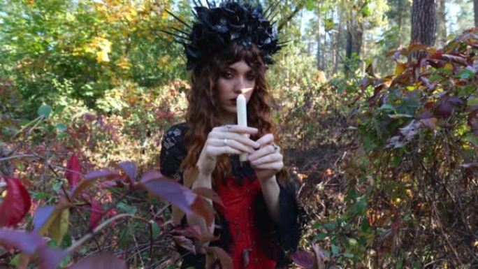 一个魔术女人站在秋天的树叶旁时，手里拿着一支燃烧的蜡烛。万圣节女人。万圣节肖像