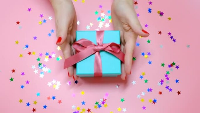 女性双手拿着粉色背景上的礼品盒，顶视图